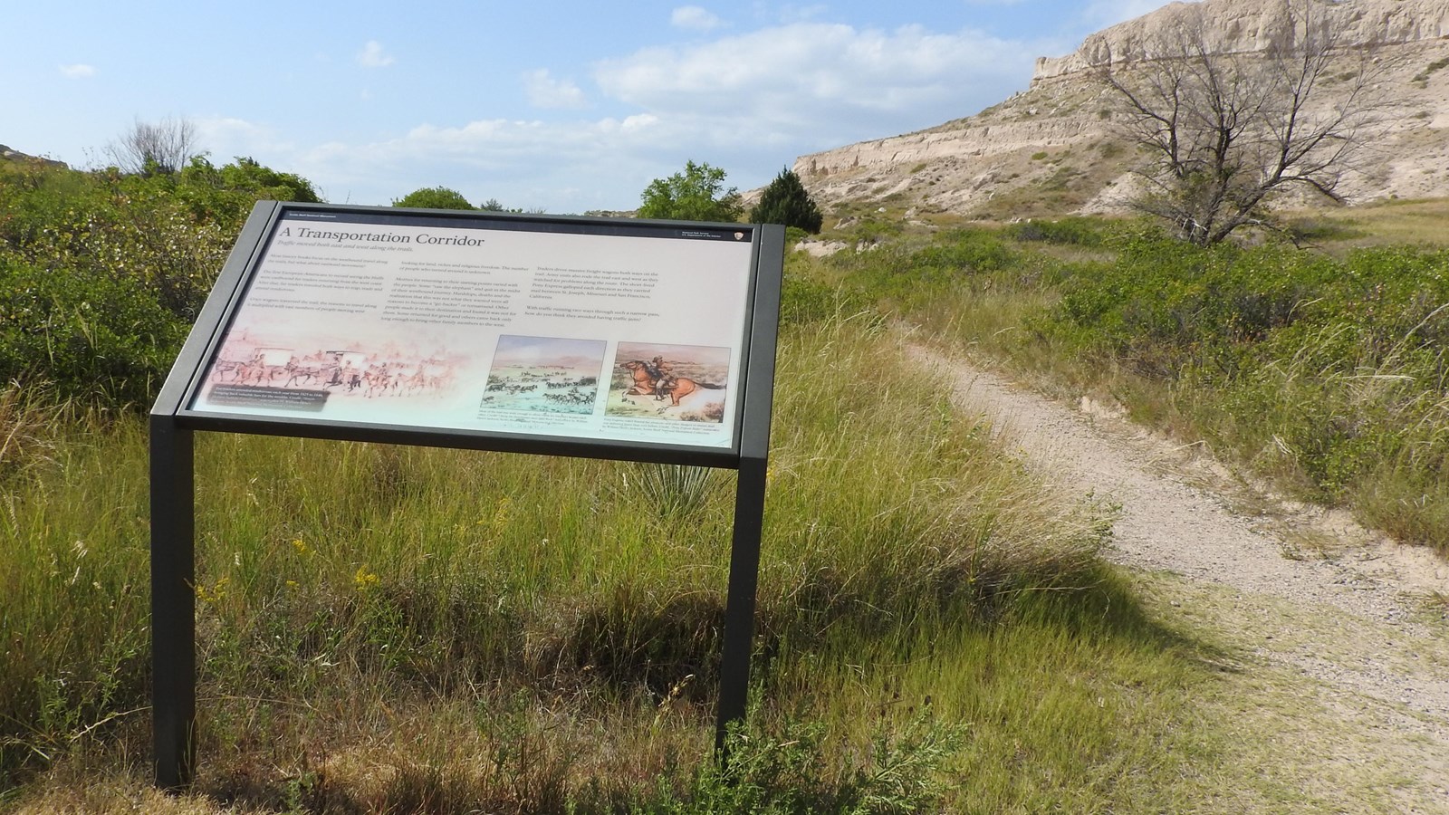 A wayside panel sits to the left of a gravel trail.
