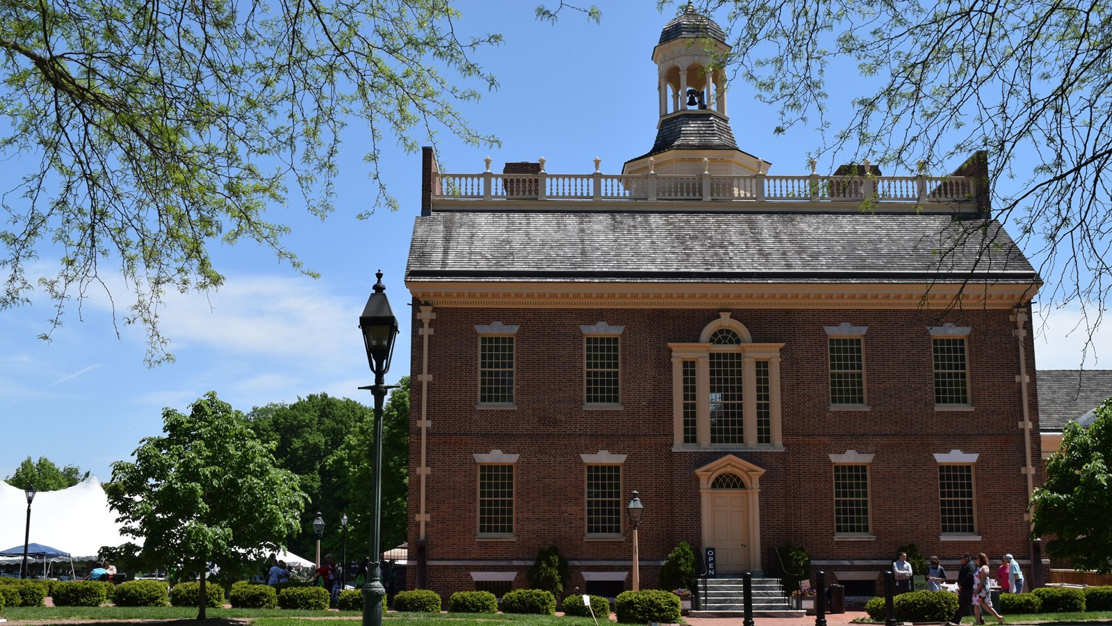 A red brick building with a large porch and cupola on top. 
