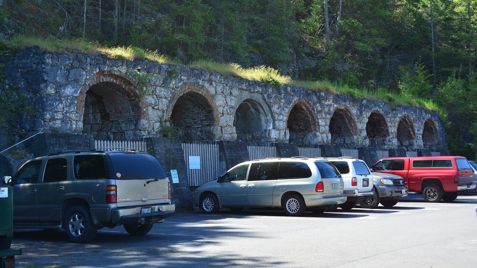 a row of tall brick structures with circular gaps. A line of cars is parked in front of them