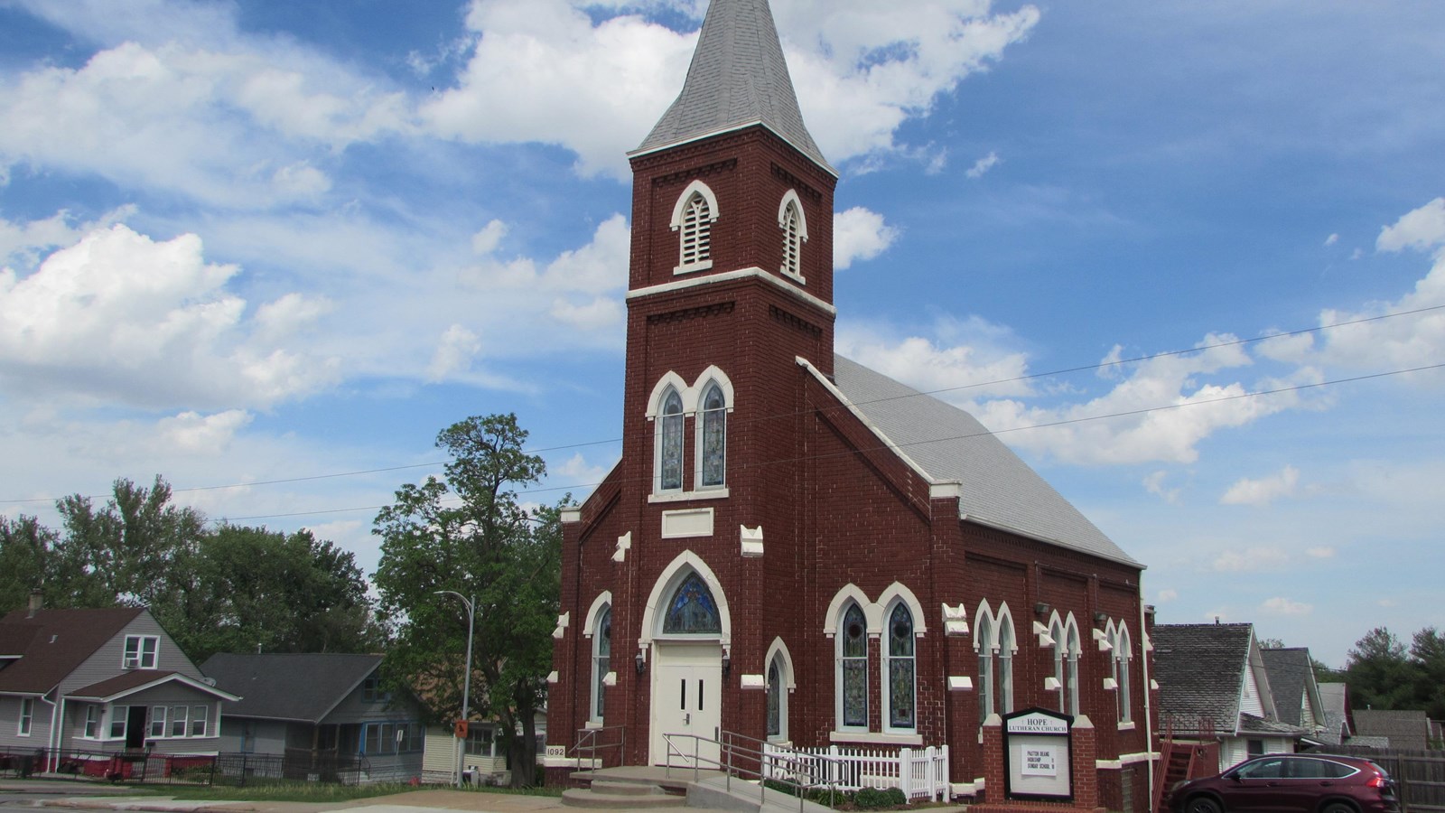 Brick, Gothic Revival church. Gabled end, center steeple and entrance. Pointed-arch windows