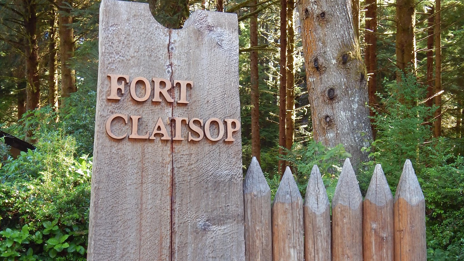 A tall wooden sign reading \'Fort Clatsop\', logs are carved to its side to look like fort walls