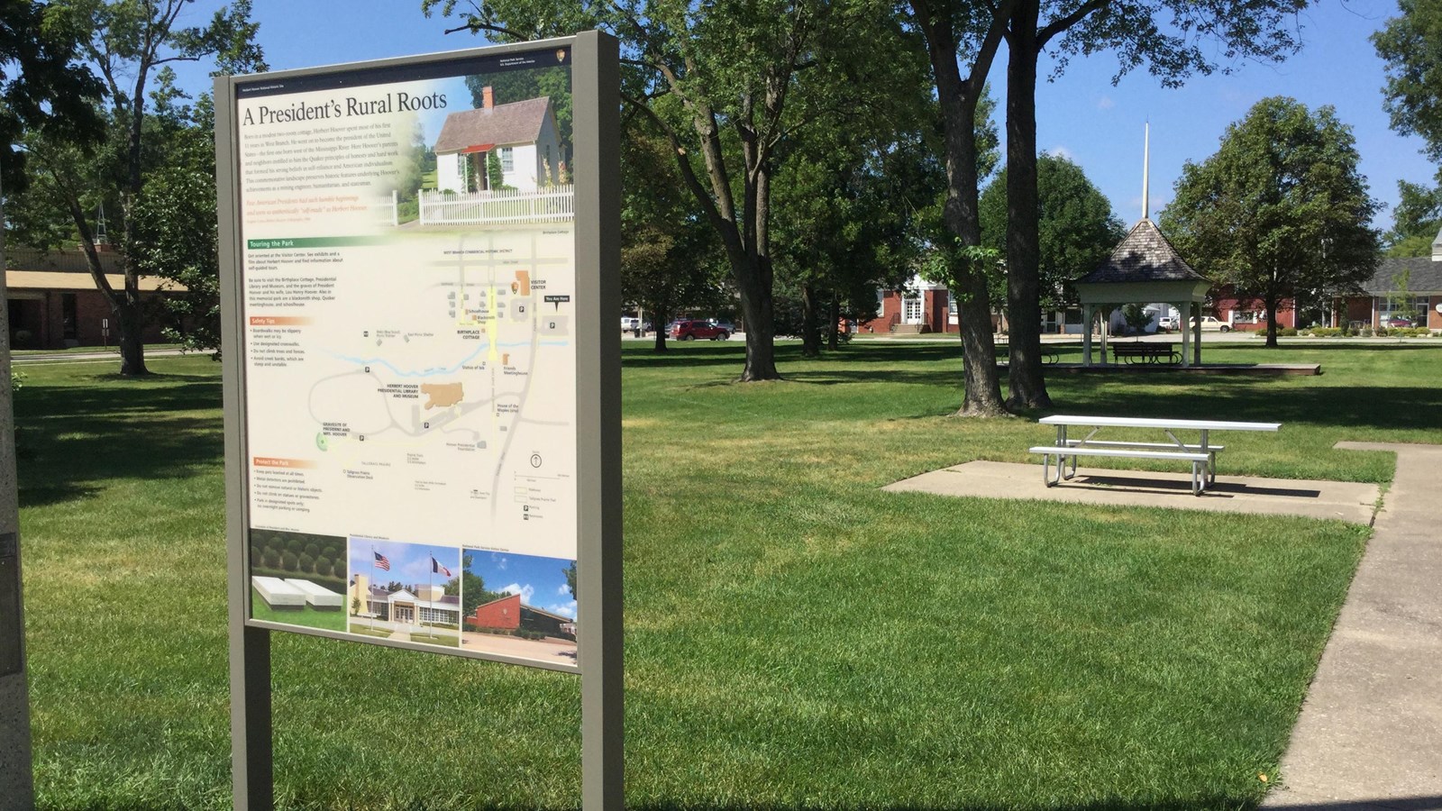 An upright outdoor exhibit panel in a park displays a map, photos, and interpretive text.