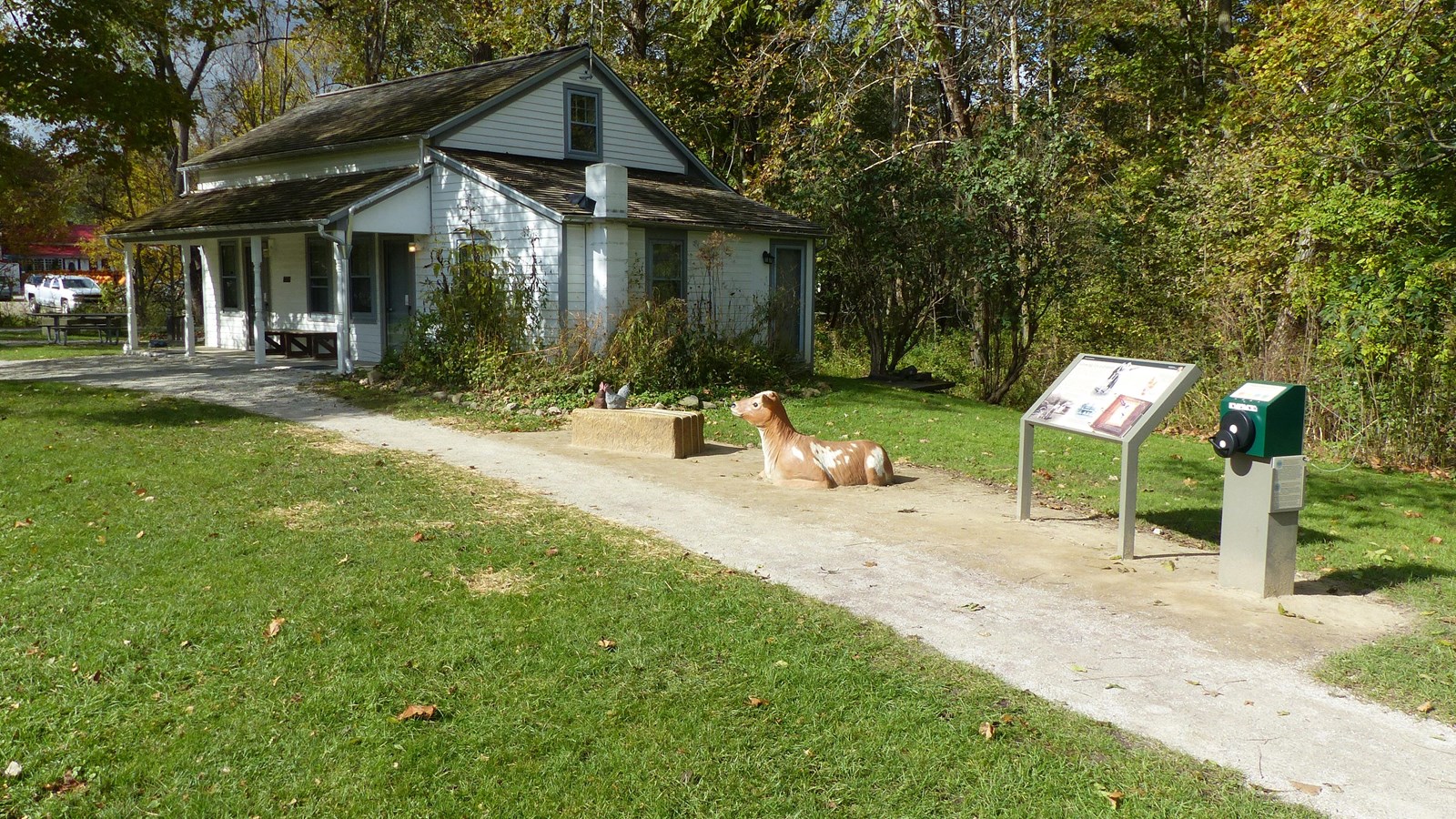 : Exhibits beside a small white house with a porch include statues of a seated calf and chickens.