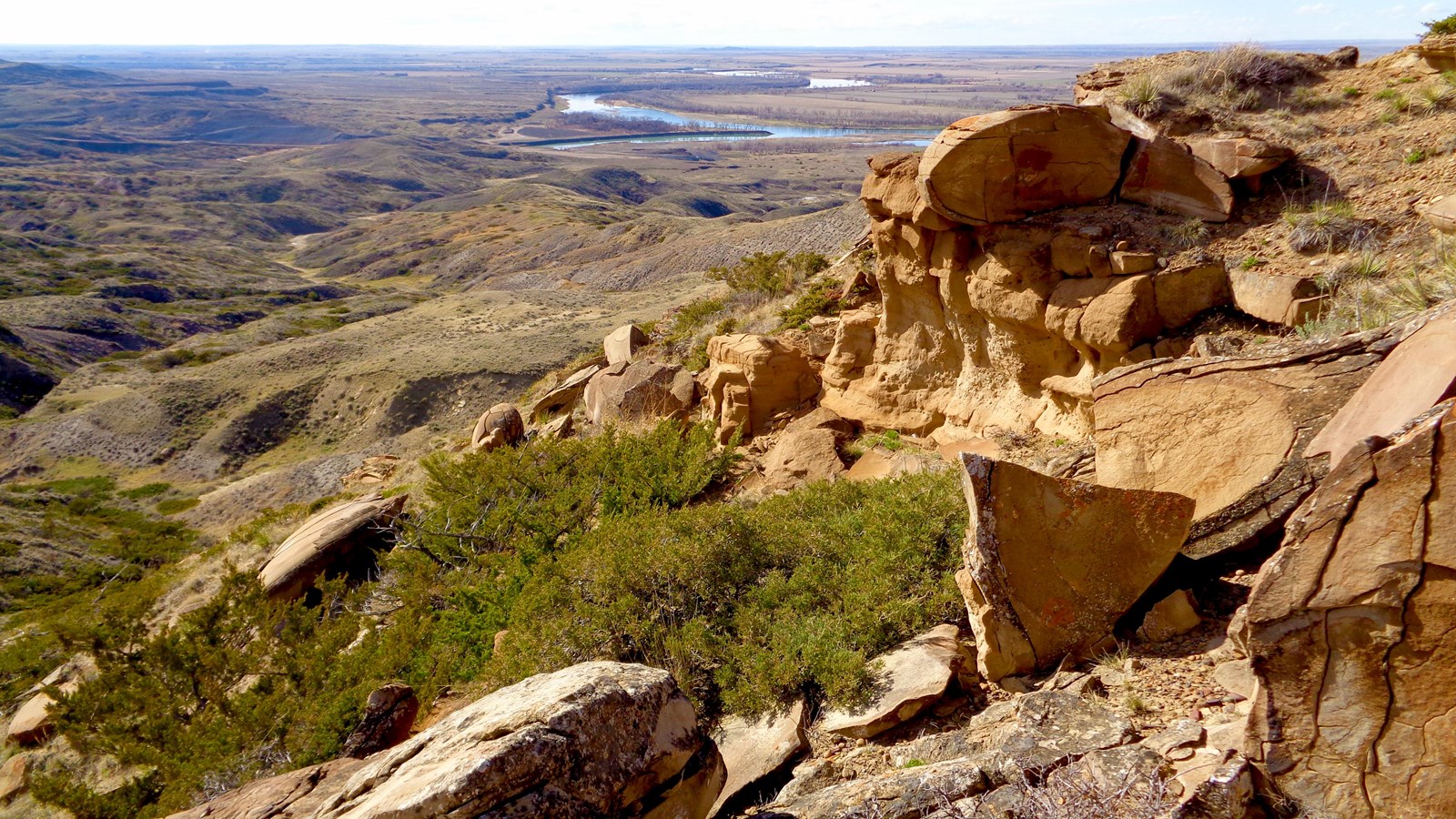 view from a cliff with brown rocks overlooking a river confluence