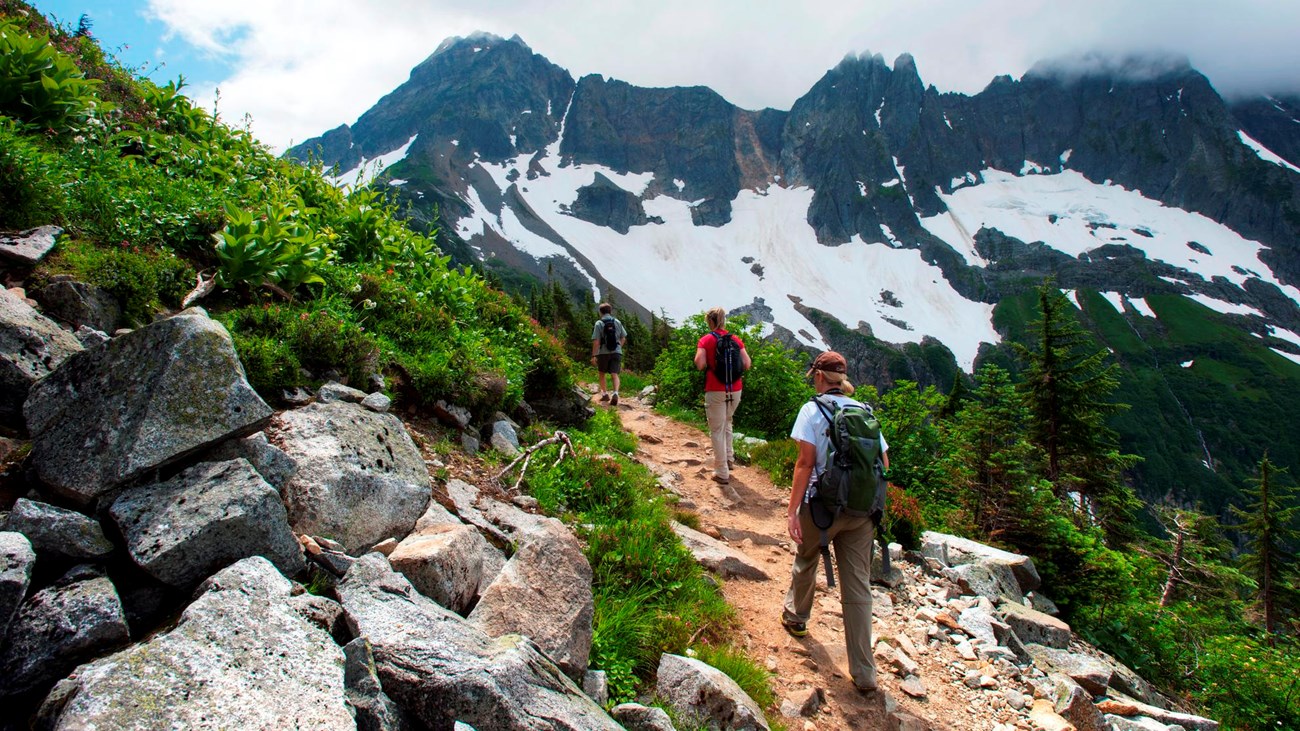 Two hikers walk along a trail with mountains in the distance.