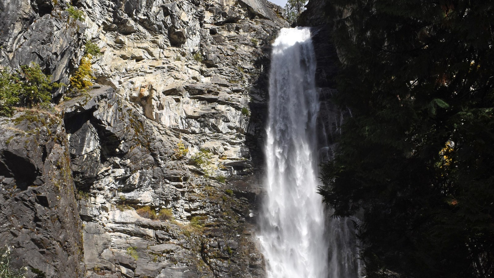 A thin waterfall drops down a gray cliff face.