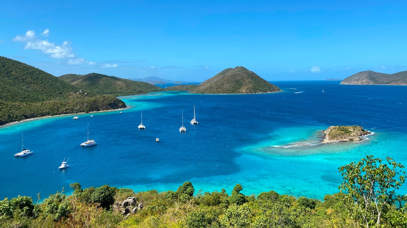 Distant boats dot turquoise water of varying shades on a brilliantly sunny day.