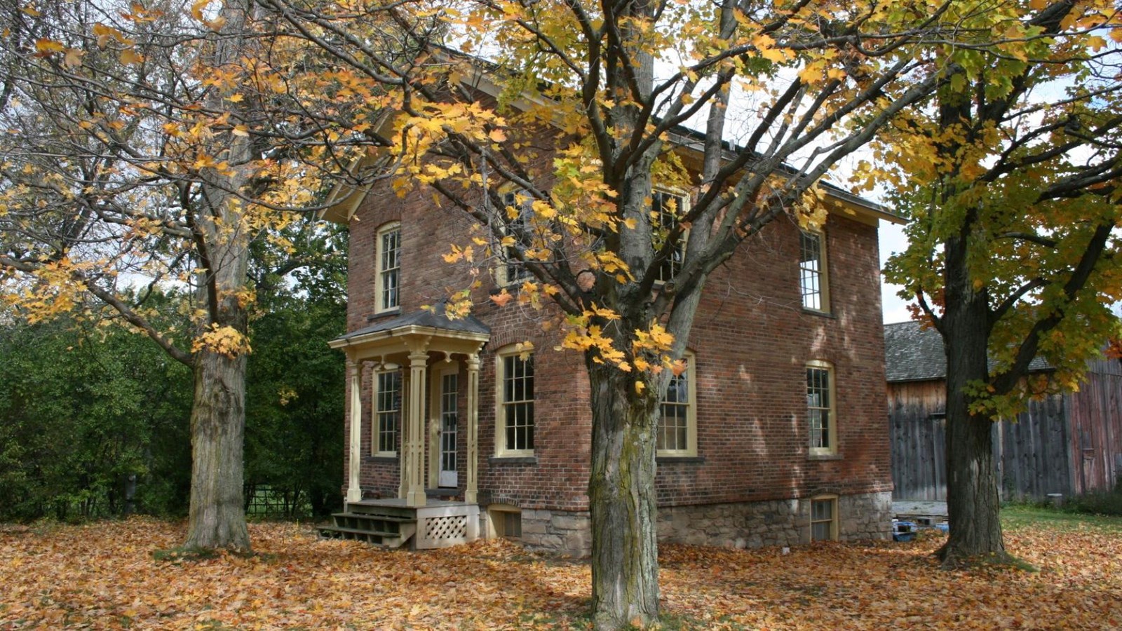 The front of a brick two-story house with small white columns in front surrounded by trees with fall