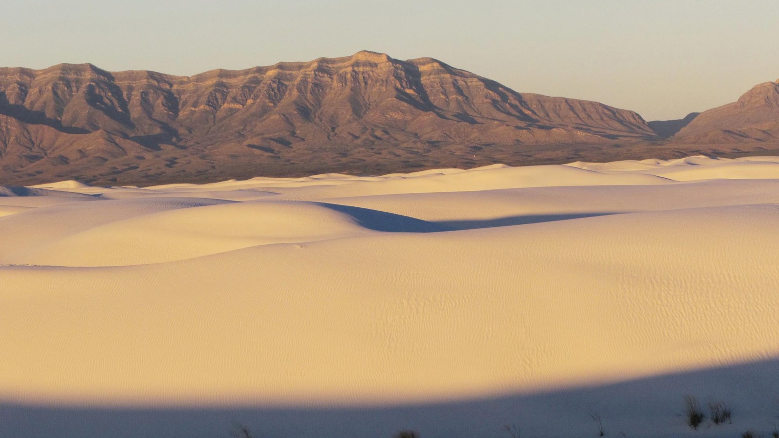 In the foreground, rolling white dunes. The San Andres Mountains sit above the dunes at sunrise