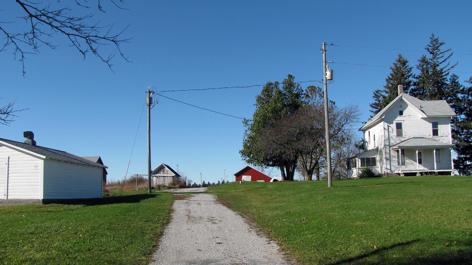 A white two-story house with multiple sheds overlooks the park and tallgrass prairie.
