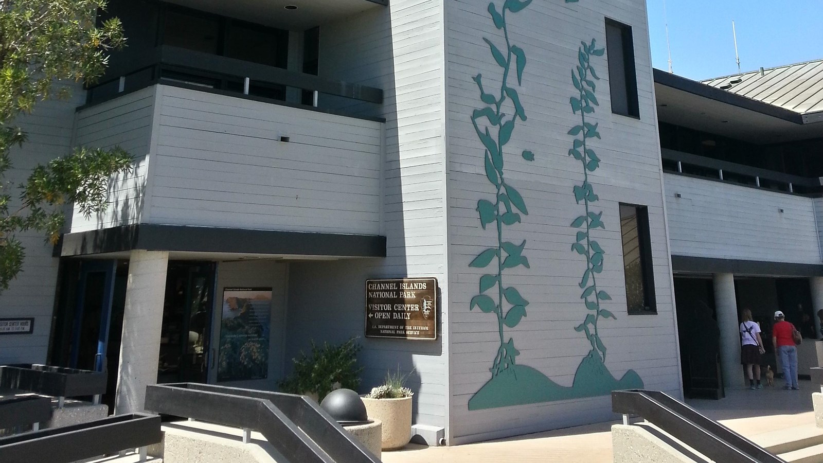 Large tower painted grey with blue-green kelp metal cutout mounted to its wall.