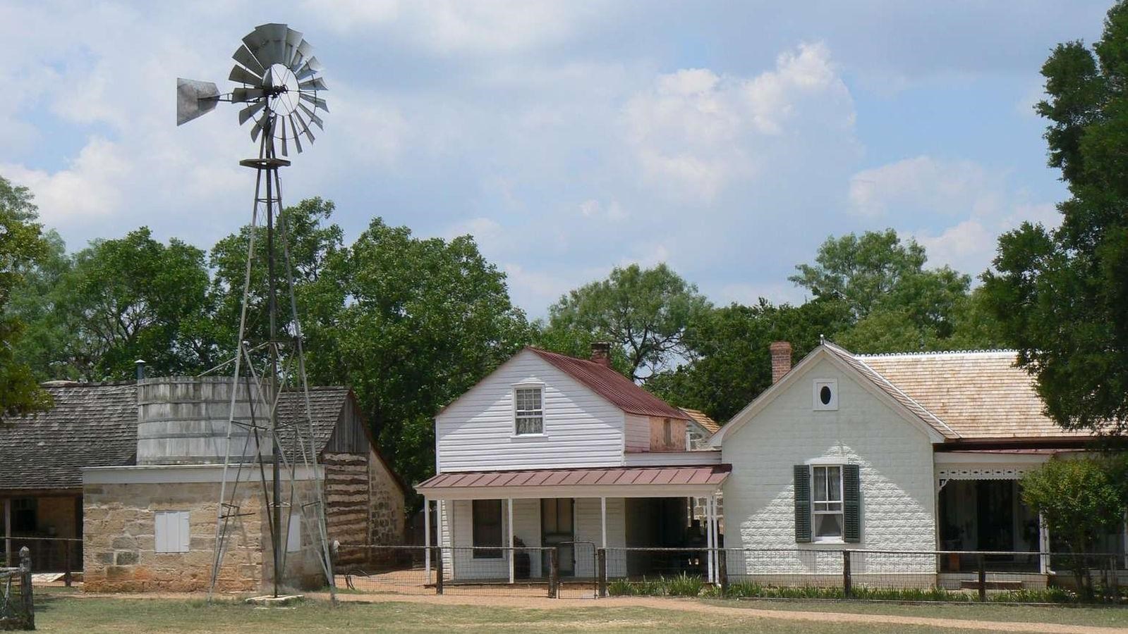 A windmill towers over a white frame farmhouse dating circa 1918.