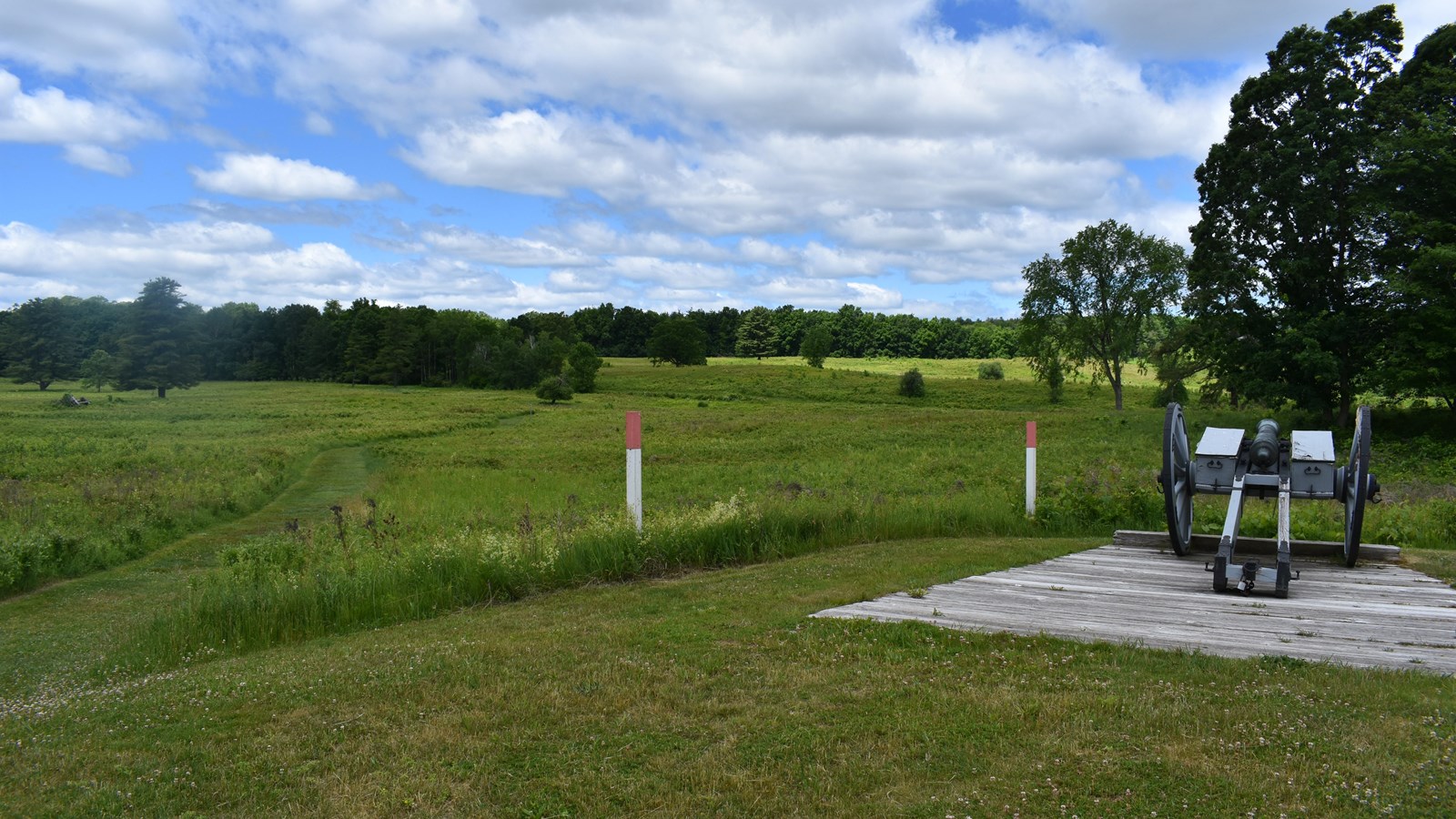 A cannon rests on a concrete pad, overlooking a grass covered field.