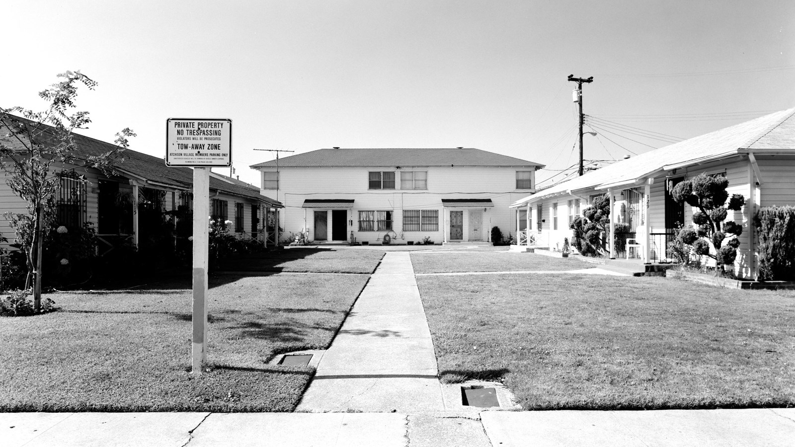 Sidewalk leads up to a two story historic home, with one story houses on the side.