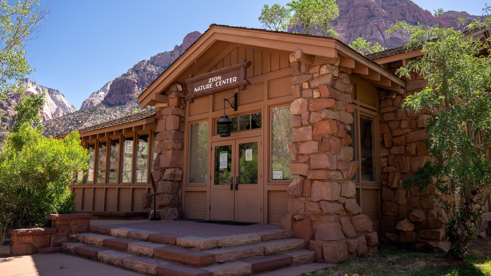 A wood-and-stone building stands in the bottom of a large sandstone canyon.