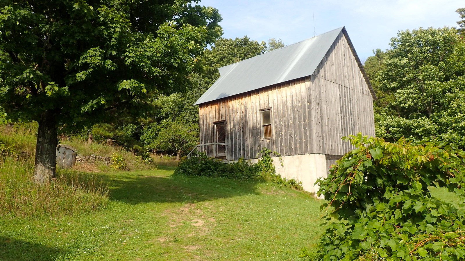 Wooden, gabled building with concrete foundation nestled on hill surrounded by trees