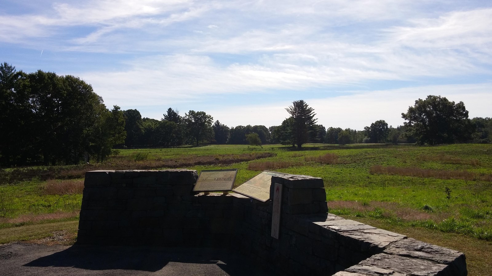 Stone walled overlook with informational signs overlooking a grassy field.