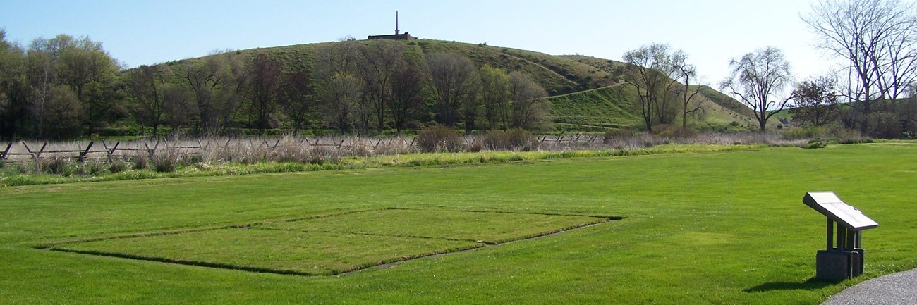 trail passing an informational sign with a monument on a hill in the background