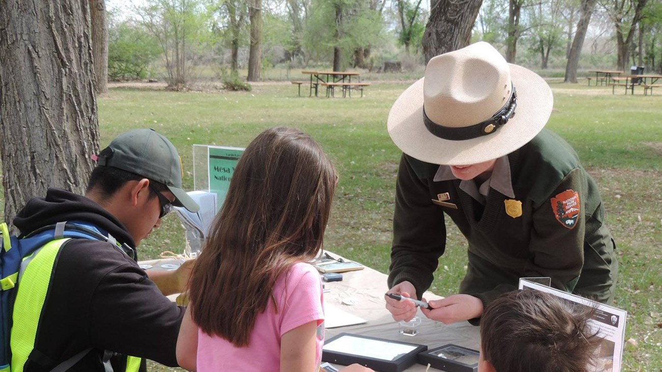 3 children work at a table in front of a park ranger.