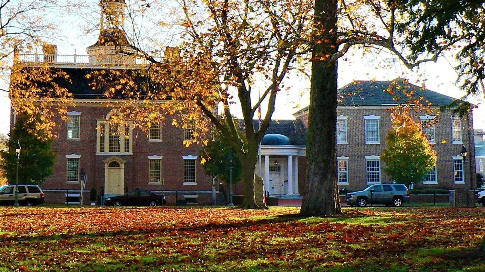 Vibrant yellow, orange and red leaves lay on the ground in front of a colonial court house. 