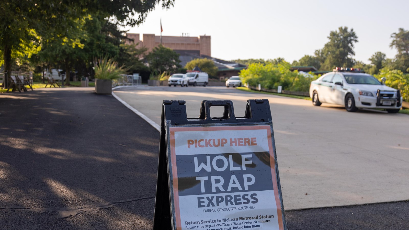 A-frame sign with bus service information on side of roadway with Filene Center in the background