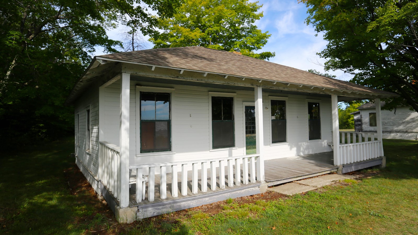 A one-story white clapboard building with a gray-shingled hip roof and a wide front porch.