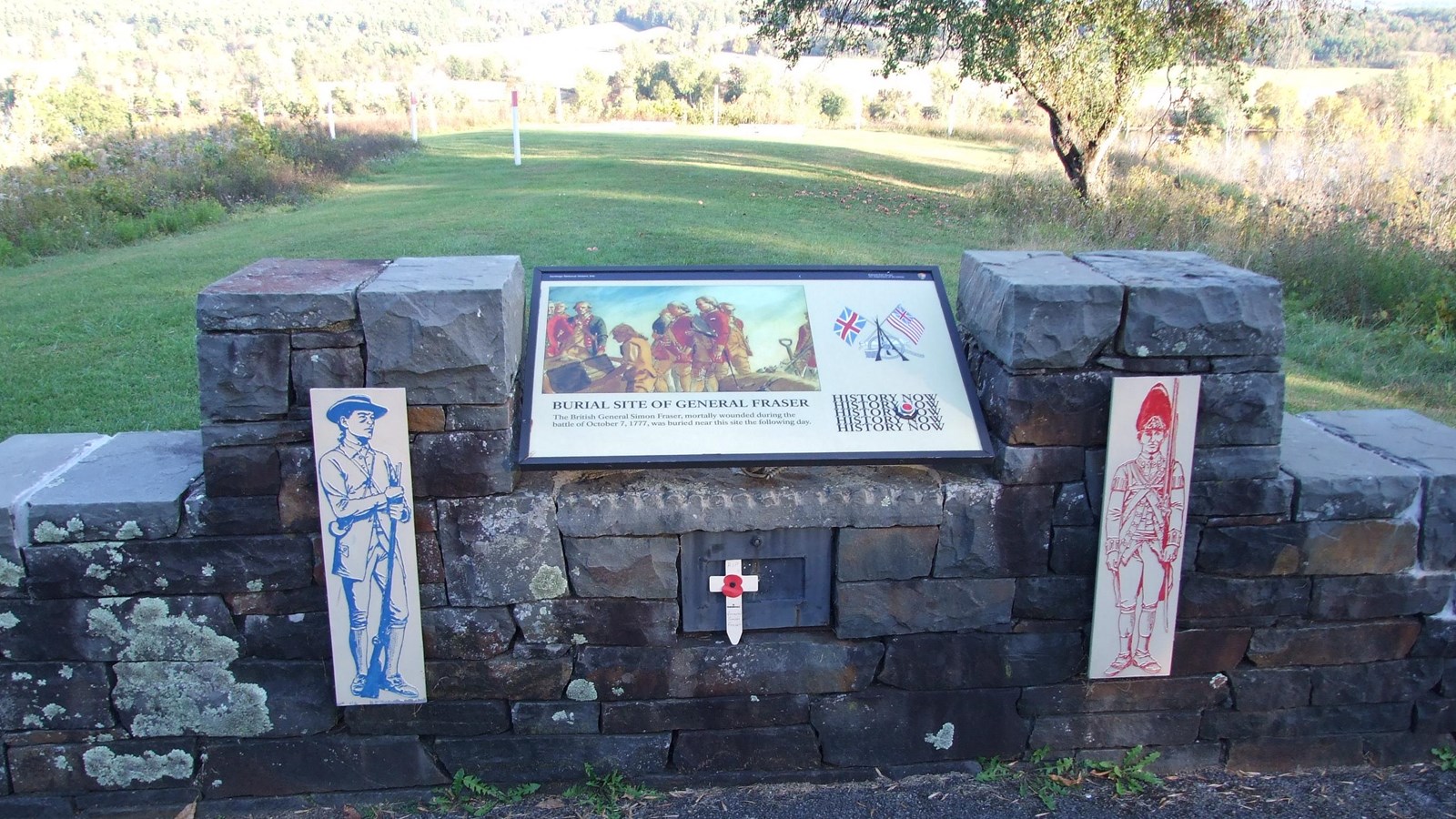 Stone wall with an informational wayside overlooking an open grassy area.