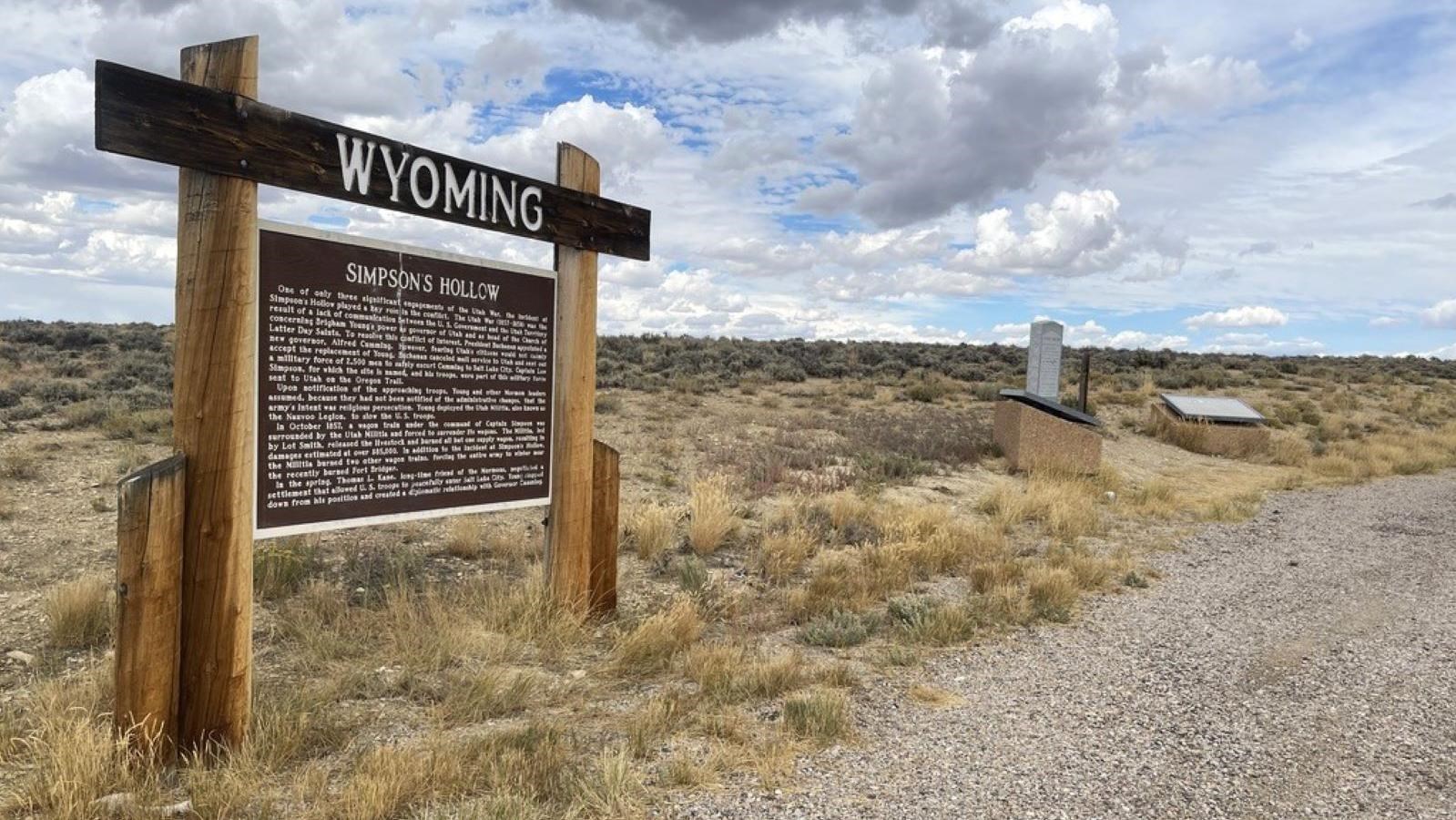 Highway turnout with Simpson’s Hollow marker, granite monument, exhibits, and desert landscape.