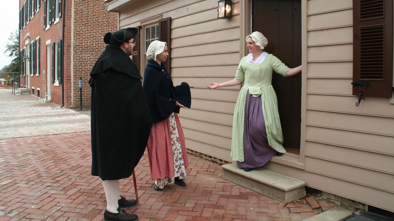 A women welcomes two people inside a small cottage. 