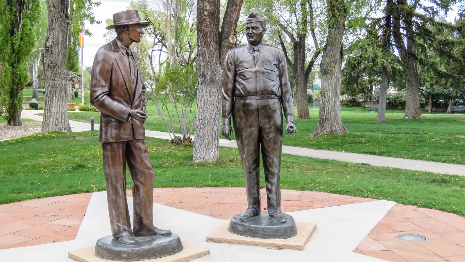 Bronze statues of two men stand on a concrete pad
