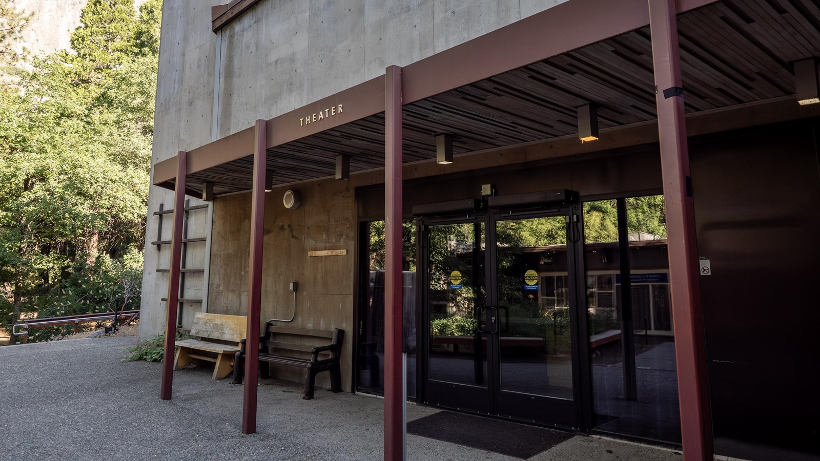 A concrete building with steel beams that create a covered entry over glass double doors