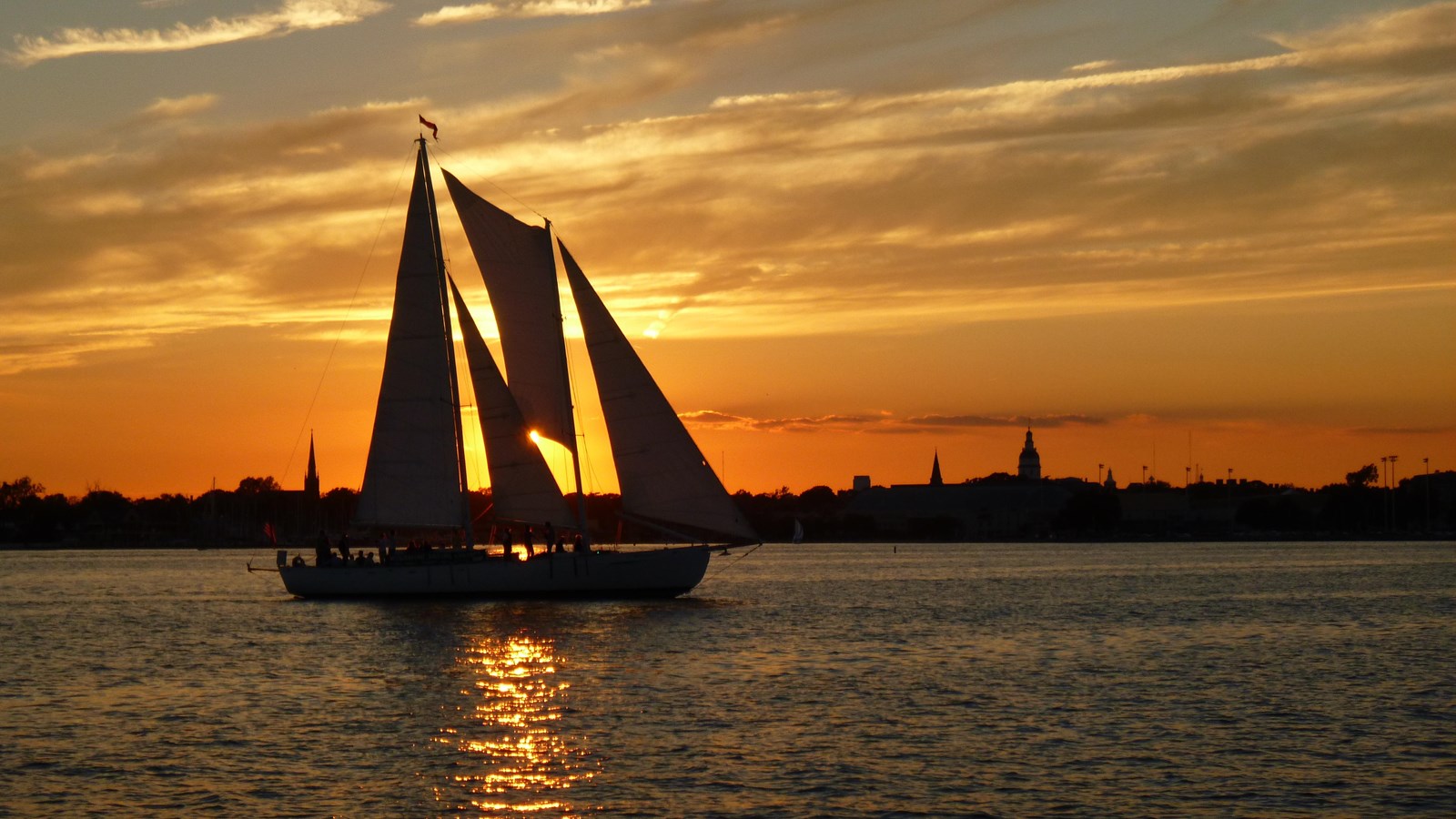 Sailboat silhouetted against a sunset with the Annapolis city skyline in the background.