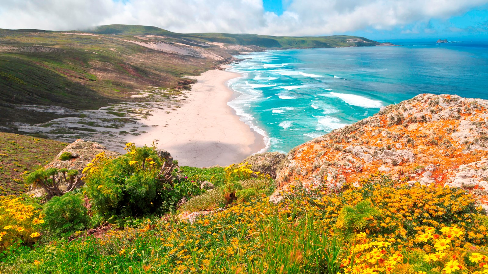 High rocky point looking down onto large white sand beach.