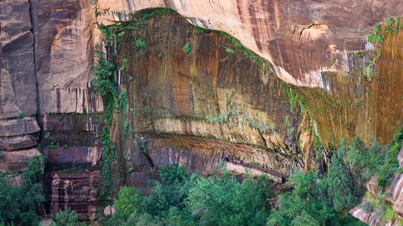 A large, arch shaped alcove streaked with dark shades of orange on red rock.