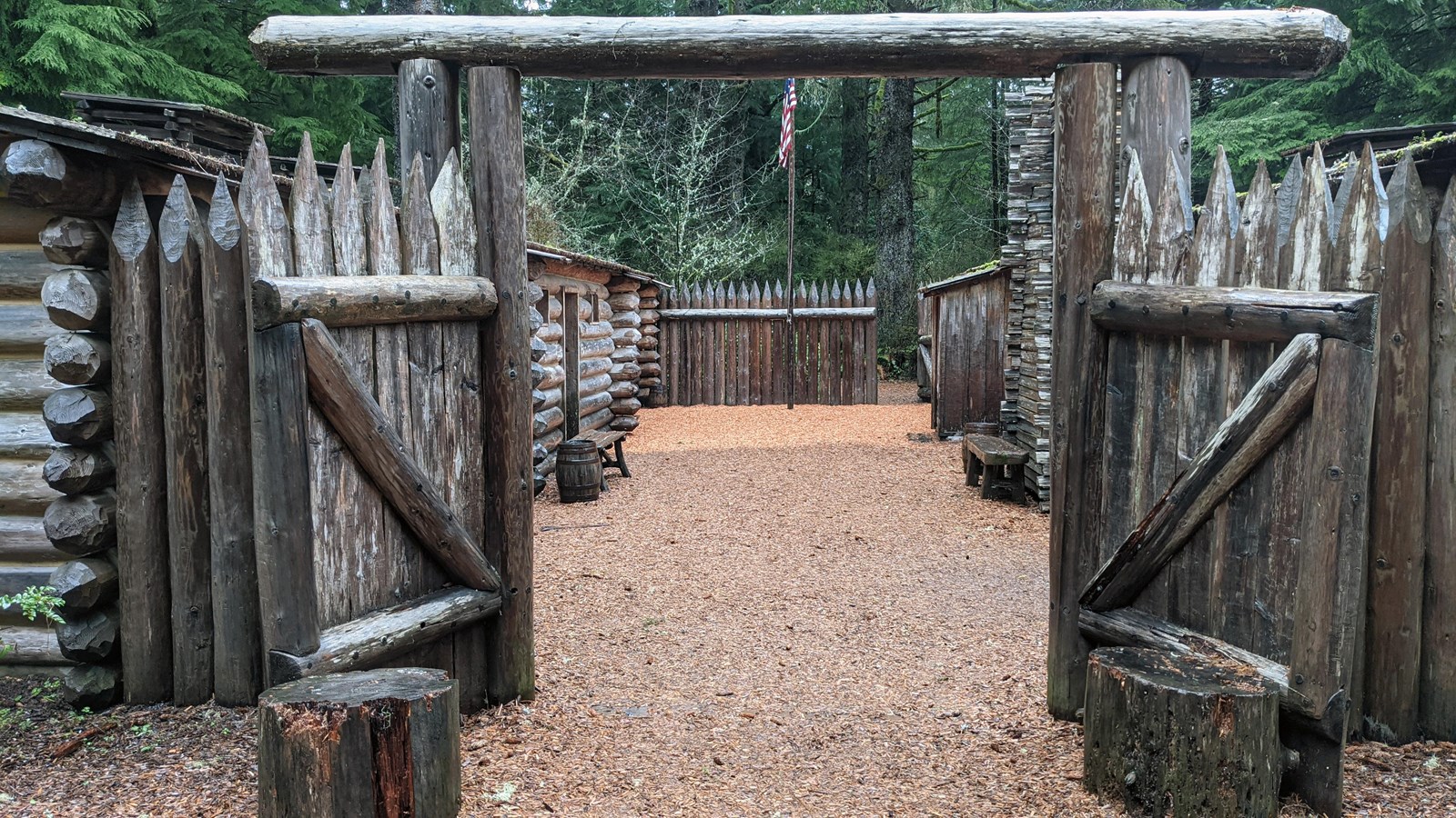 Two large swinging wood gates, sitting open, are surrounded by spiked logs.