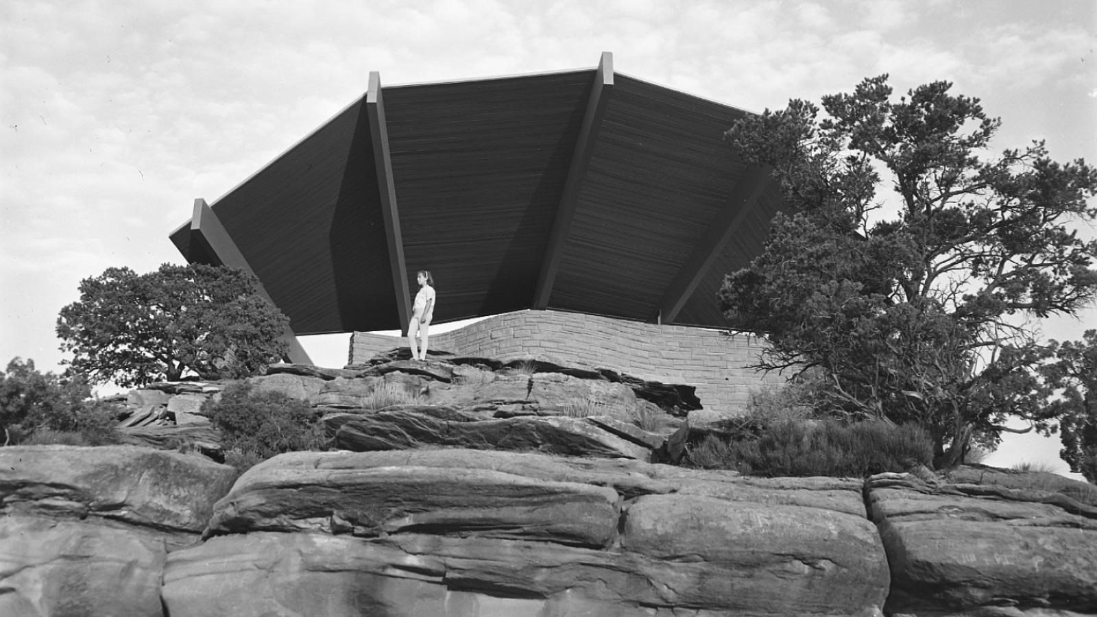 Sandstone brick shelter with cantilevered wooden roof fanning out above it.