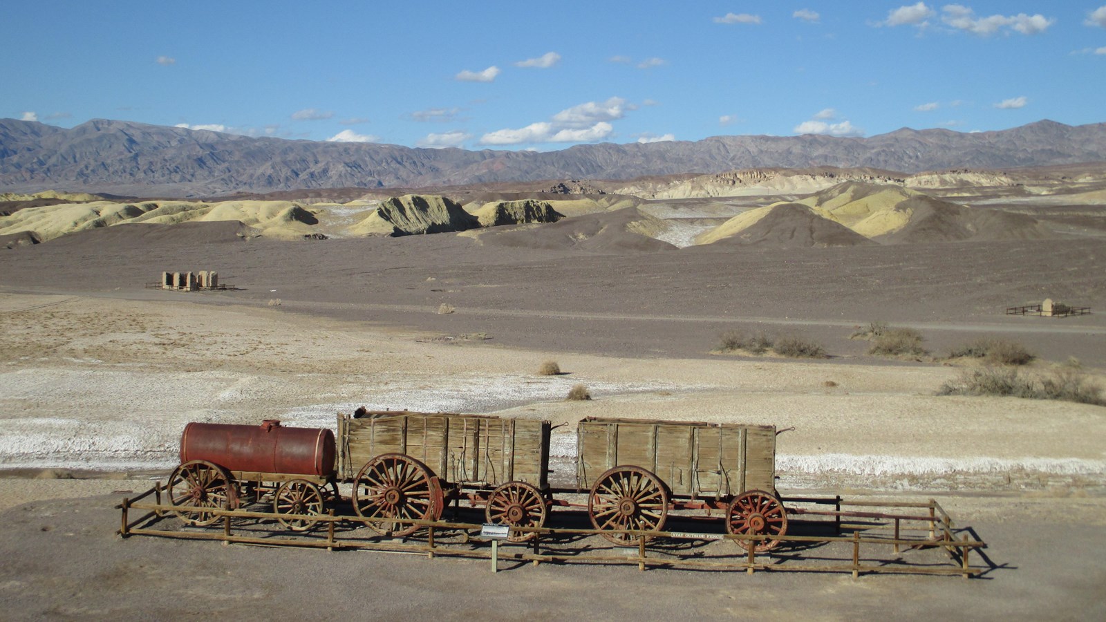 A large old double 20 Mule Team Wagon and water tank with yellow hills in the background.
