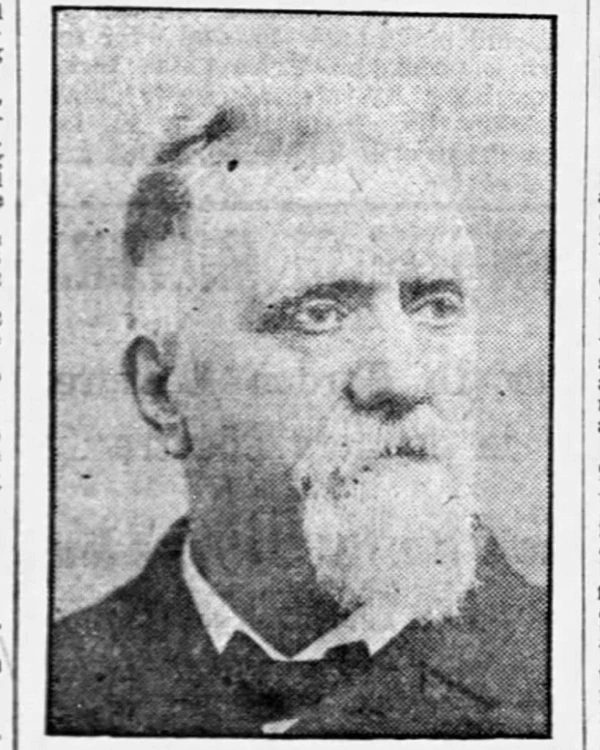 Black and white newspaper photo of a man with a white beard and mustache wearing a suit.