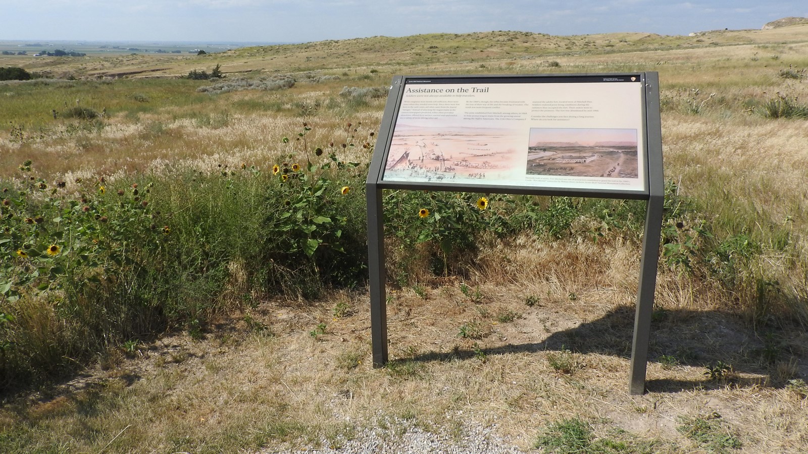 A wayside panel is located at a view overlooking a series of slopes and ravines.