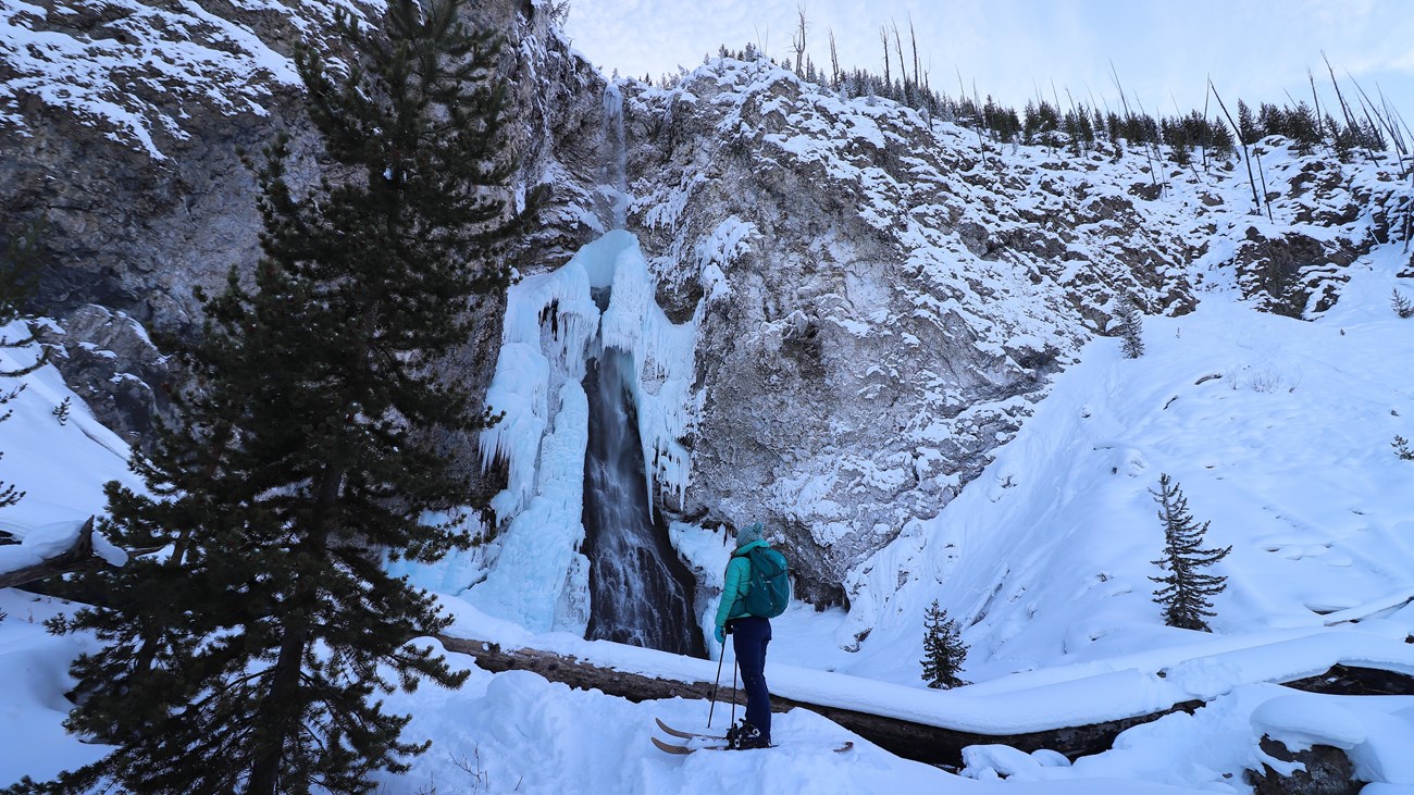 A skier looks up at the ice formations surrounding a frozen waterfall.