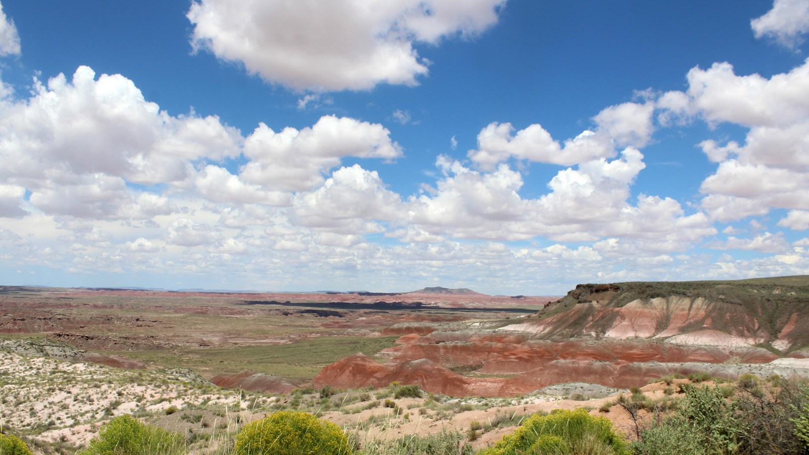 Red badlands under a blue and partially cloudy sky.