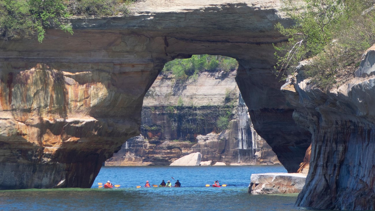 Group of kayakers under large sandstone arch
