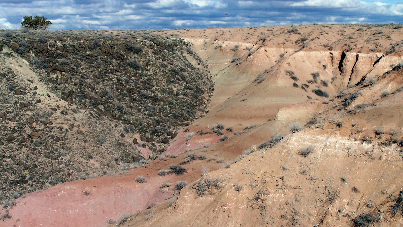 Brown and pink badlands topped with dark volcanic basalt under a cloudy sky.