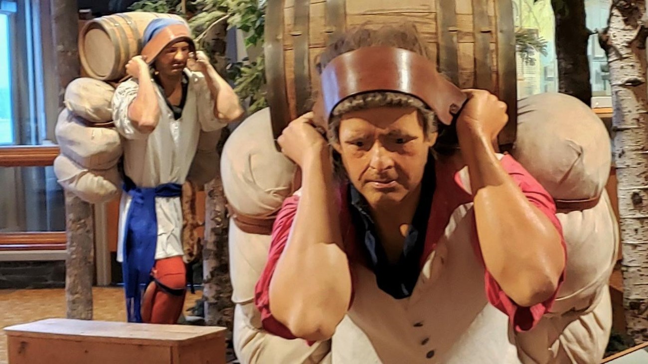 Mannequins dressed in historic clothing carrying heavy looking bales of trade goods.