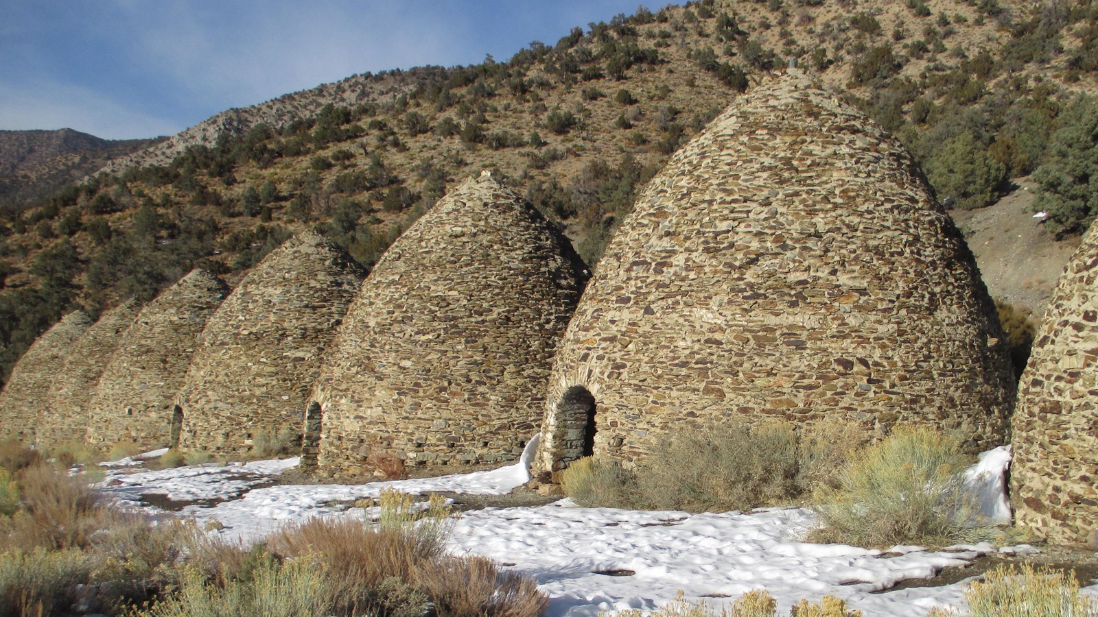 Stone and mortar beehive structures in a row in patchy snow.