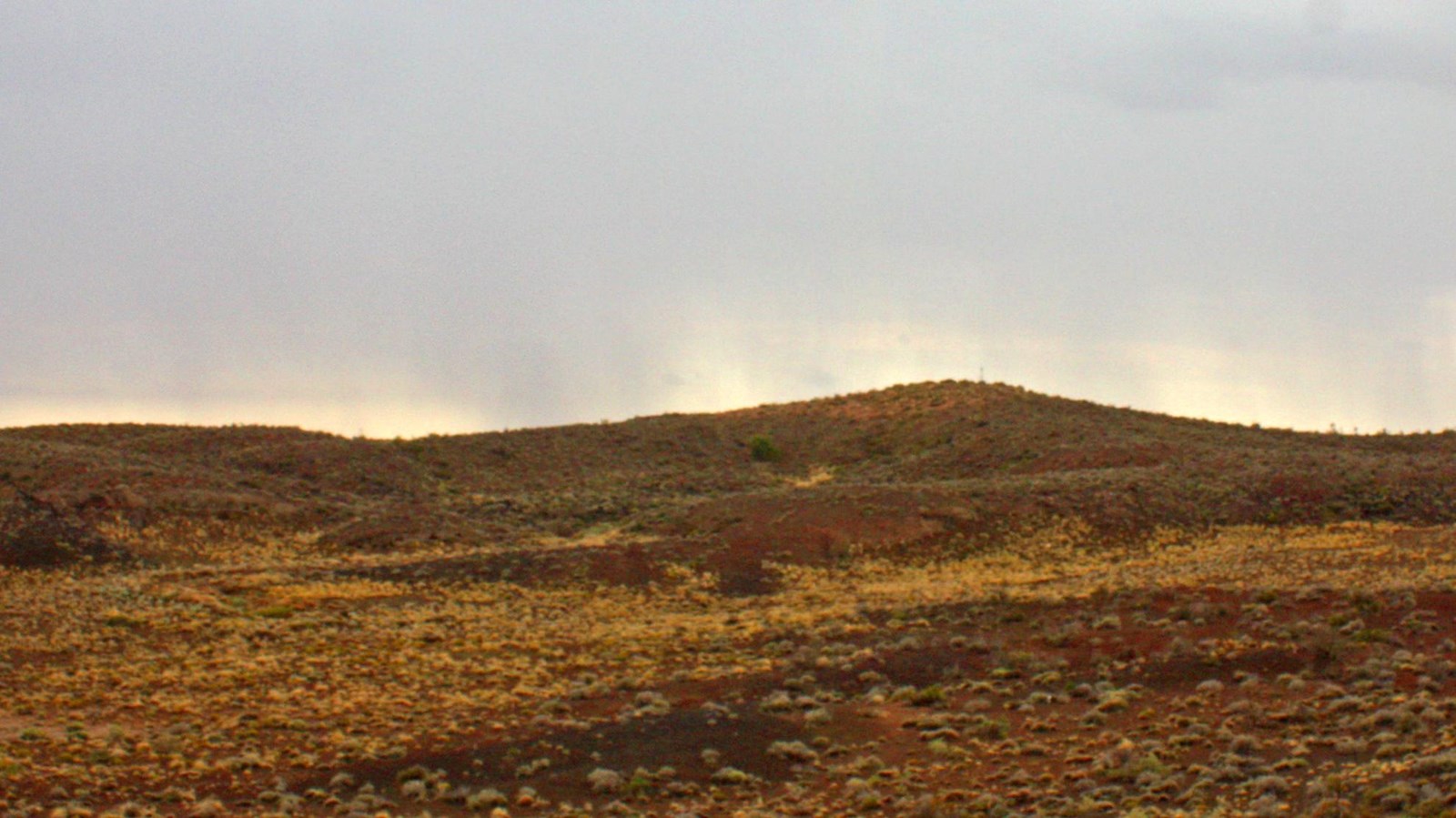 Small grass and shrub covered volcanic crater under a rainy sky.
