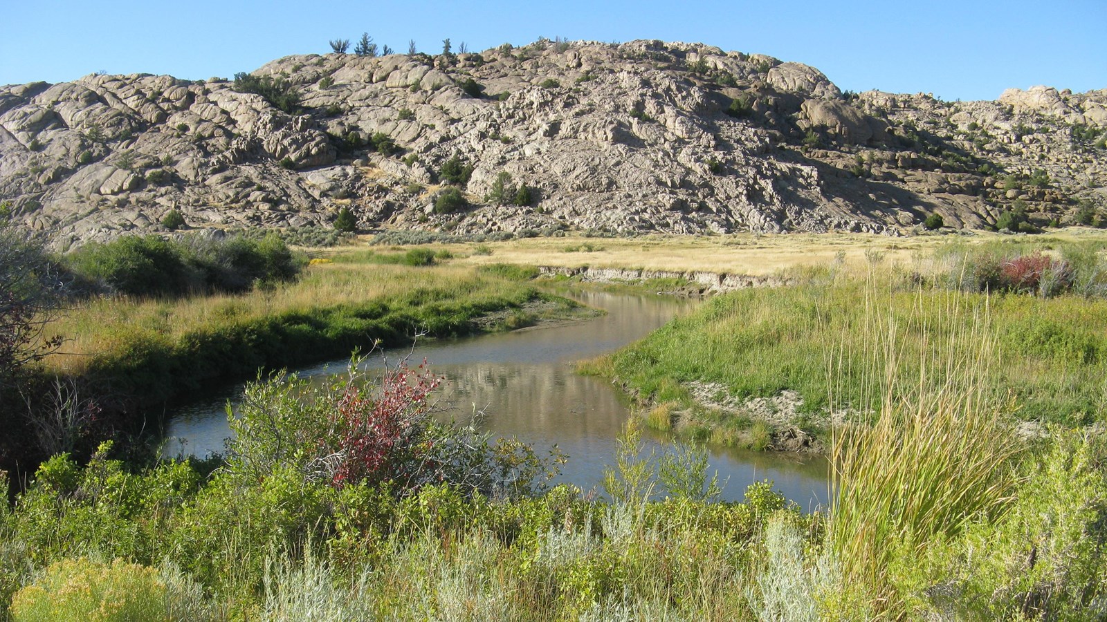 Sweetwater River winds through lush grasses, tan prairie, and cracked granite ridges.