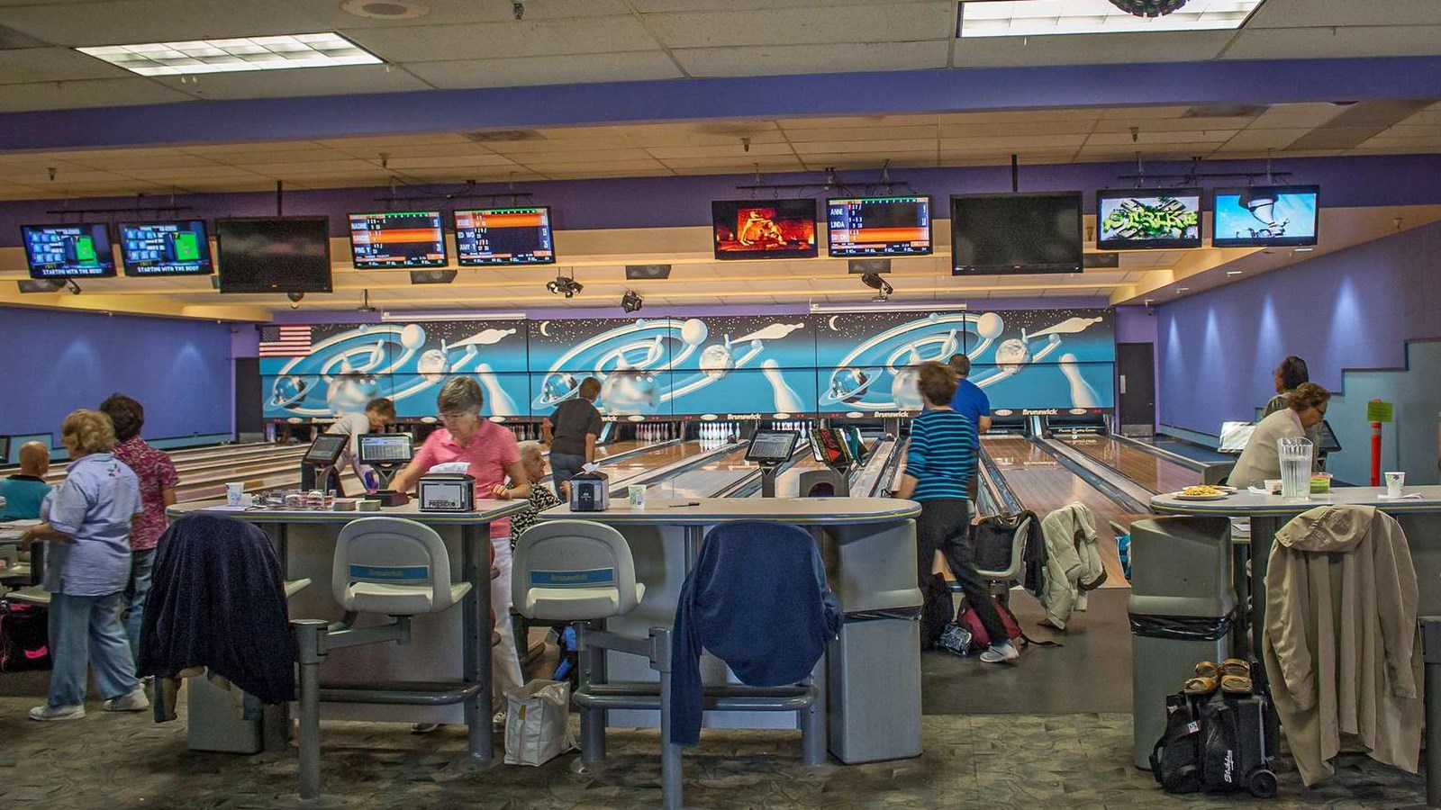 Visitors using multiple bowling lanes and enjoying snacks at the bowling alley.