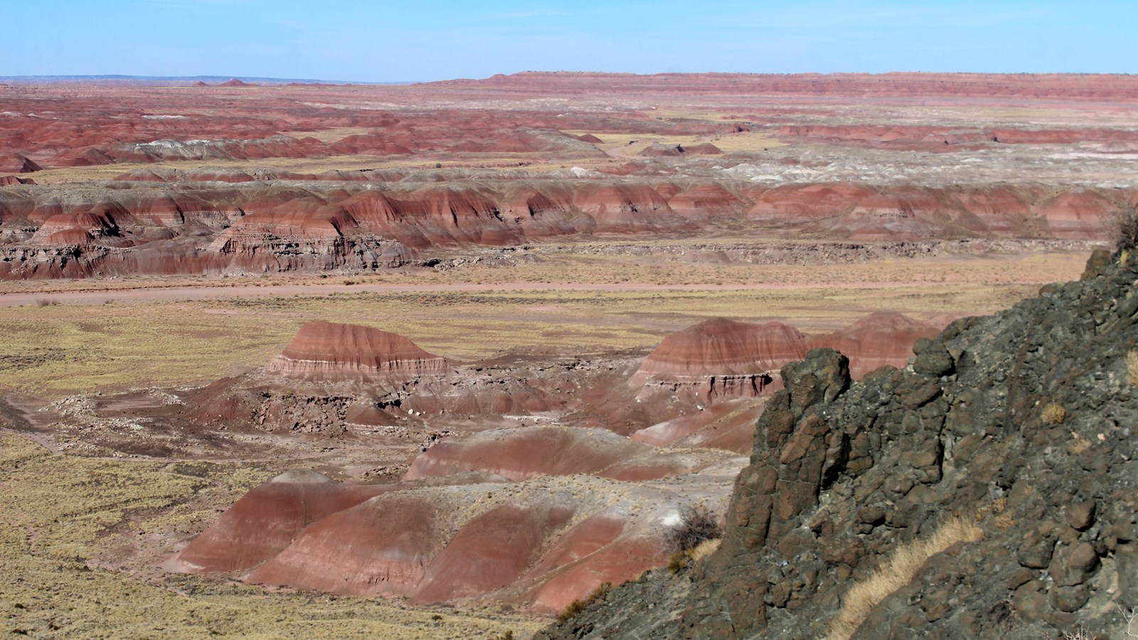 Black pillow basalt against a sunlight backdrop of red badlands and blue sky.