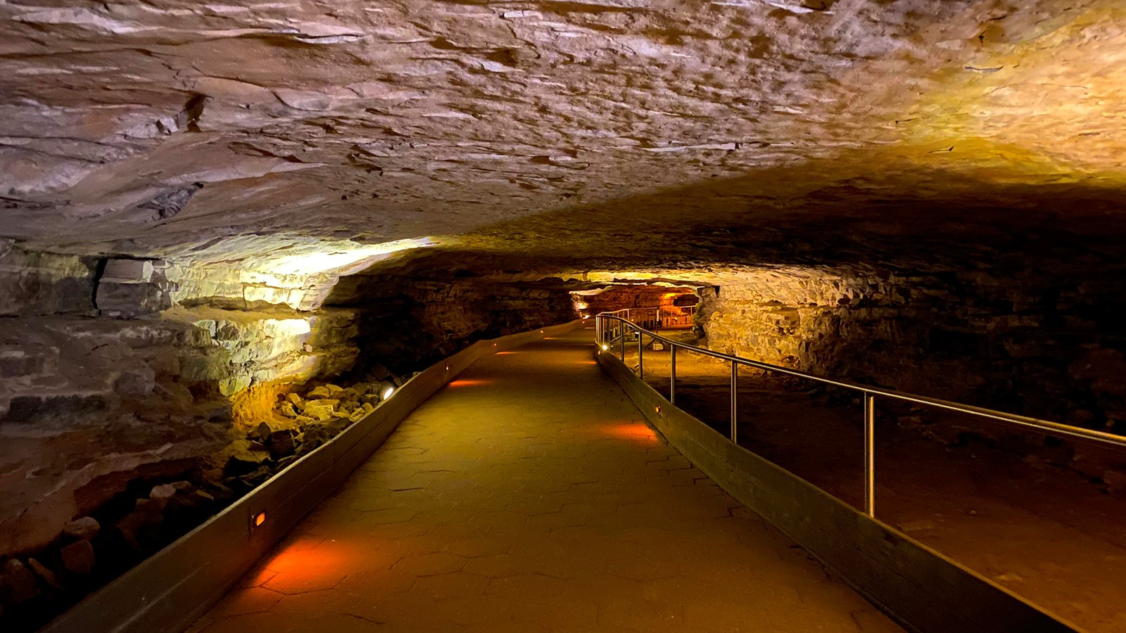 A long cave passage with a ceiling that is around 7 feet high. A metal railing lines one side.